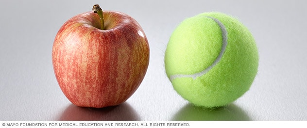 Una manzana pequeña junto a una pelota de tenis.