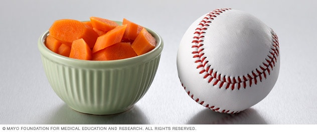 Media taza de zanahorias cocidas junto a una pelota de béisbol.