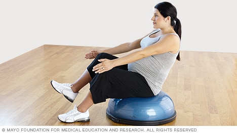 امرأة حامل تمارس تمرين الجلوس على شكل حرف (V) على قدم واحدة باستخدام جهاز التوازن