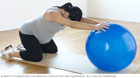 Una persona embarazada haciendo un estiramiento hacia atrás con una pelota para ejercicio.