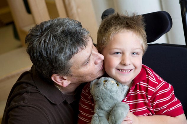 A father kisses his cheerful son between therapy exercises.