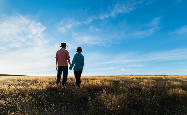 A couple stand in a field while looking at a sunset.