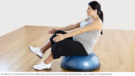 Ejercicios para el embarazo - Mujer embarazada realiza un abdominal en V con una pierna con una plataforma de equilibrio Bosu