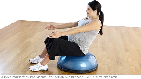 Persona embarazada haciendo abdominales en V, sentada en una plataforma de equilibrio