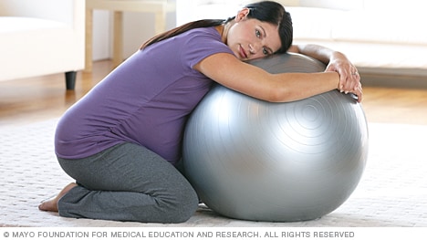 Una persona en trabajo de parto arrodillada contra una pelota de parto.