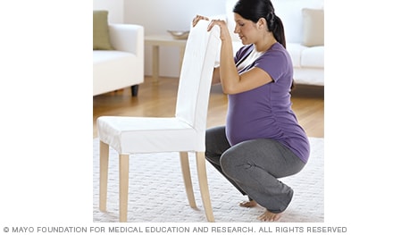 A person in labor squatting with a chair for support