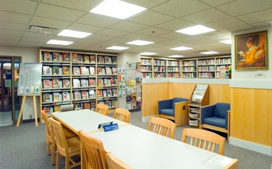 Biblioteca para pacientes en la que se muestran estantes con libros, sillas y mesas