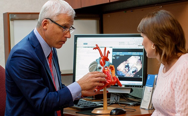 一位医生为一名患者看诊，并在讨论中使用了心脏模型和心脏图像。