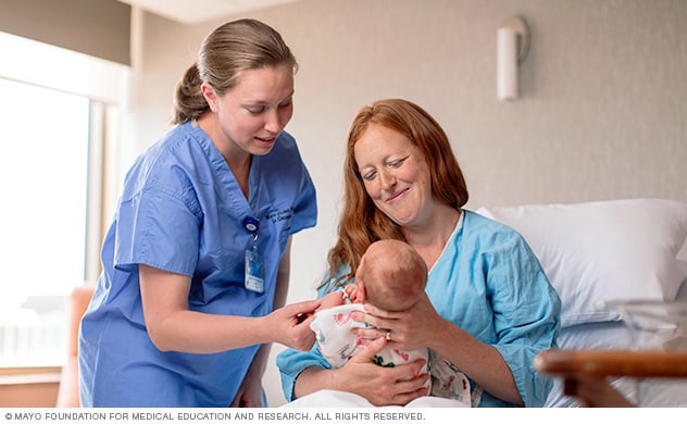 Una enfermera revisa a una madre y su bebé después del parto.