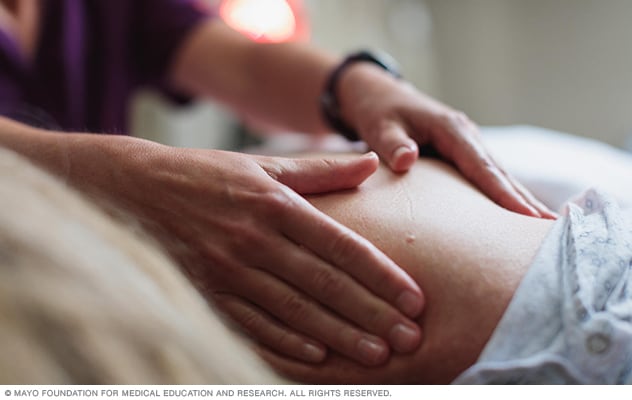 Un masoterapeuta masajea el hombro de una persona que lleva puesta una bata de hospital.