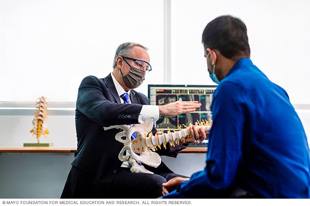 A doctor uses a 3D model of a spine to explain treatment options.