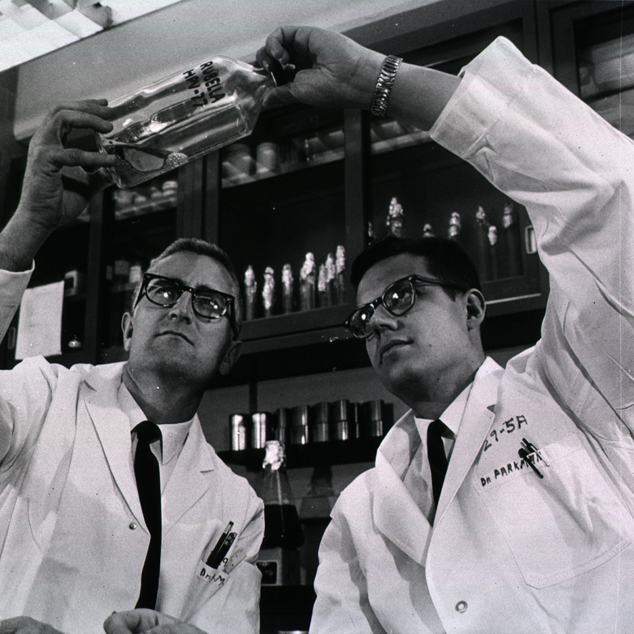 Two men who are scientists hold and look at a bottle of rubella vaccine