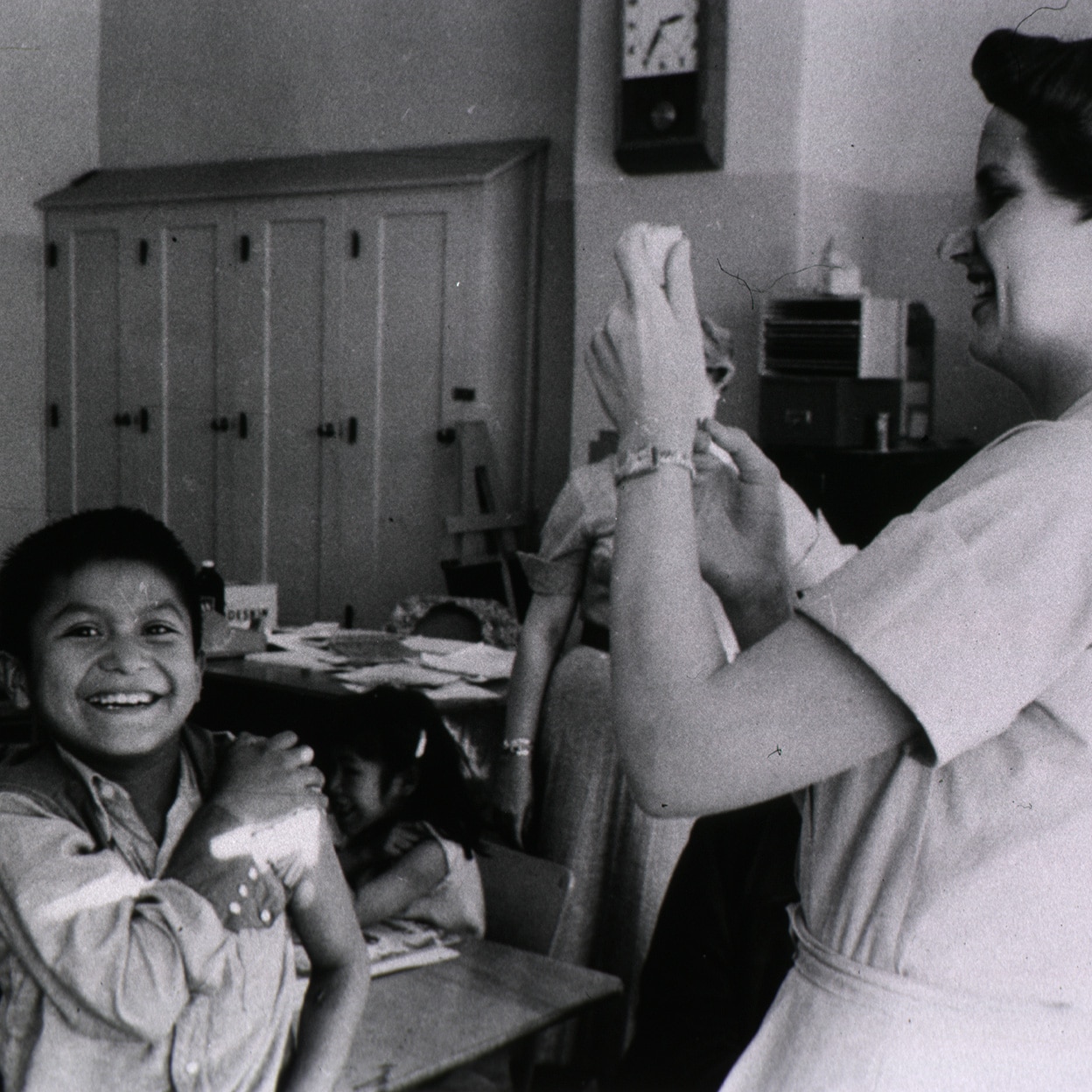 A child sits and waits for a vaccine from a nurse in a school classroom