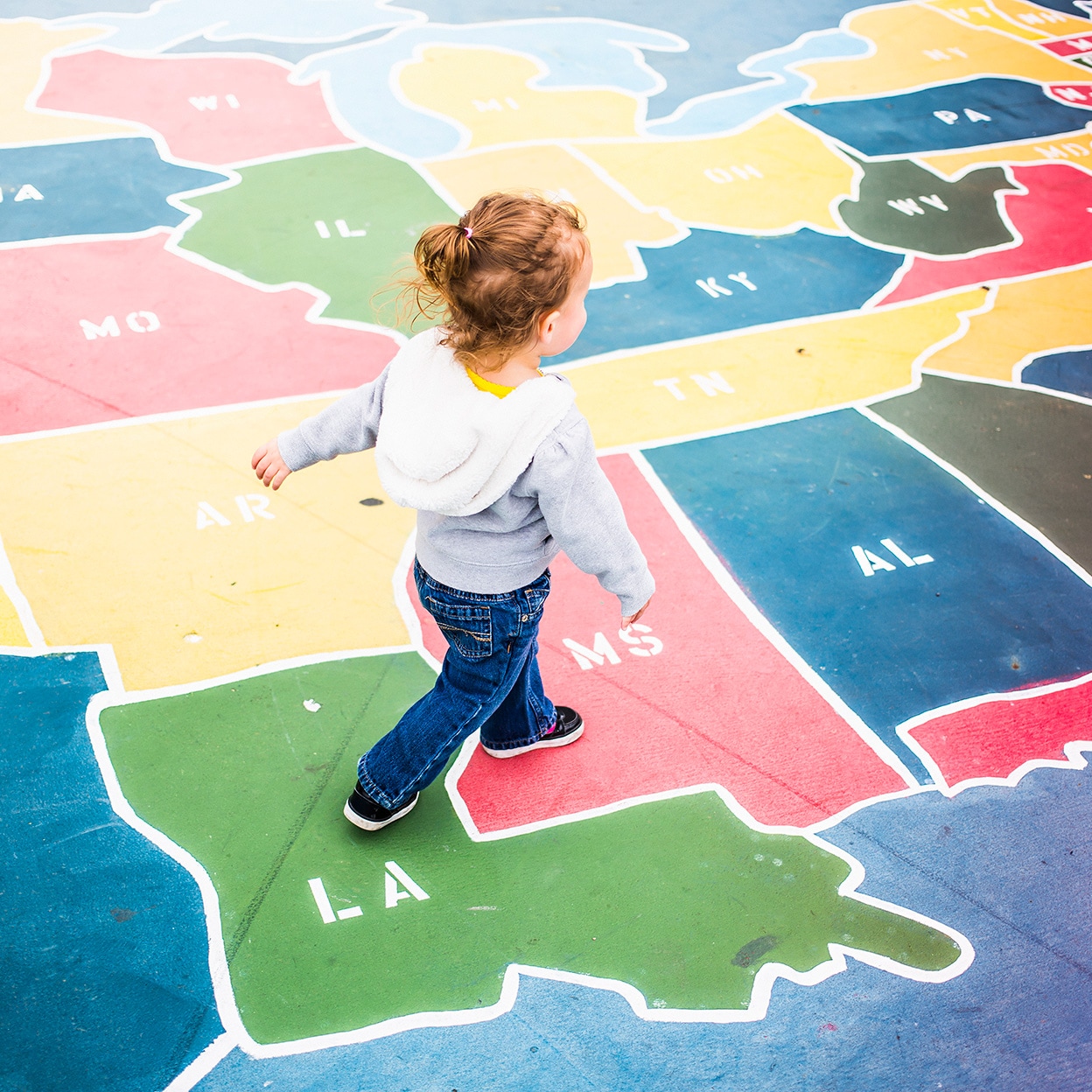 A toddler walks over a map of the U.S.A. in a playground