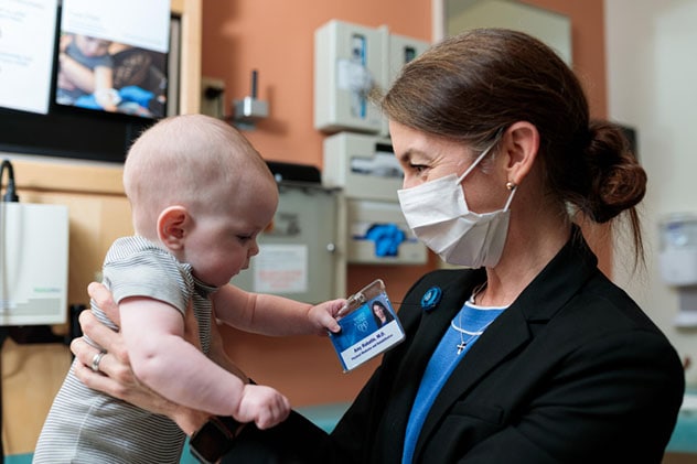 Un médico de rehabilitación pediátrica alza a un bebé y le sonríe.