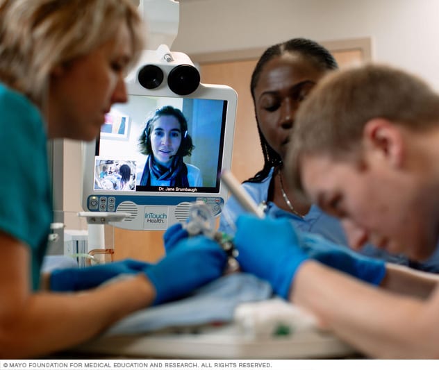 يتشاور طبيب مع فريق طبي بالفيديو أثناء إجراء عملية على طفل حديث الولادة.
