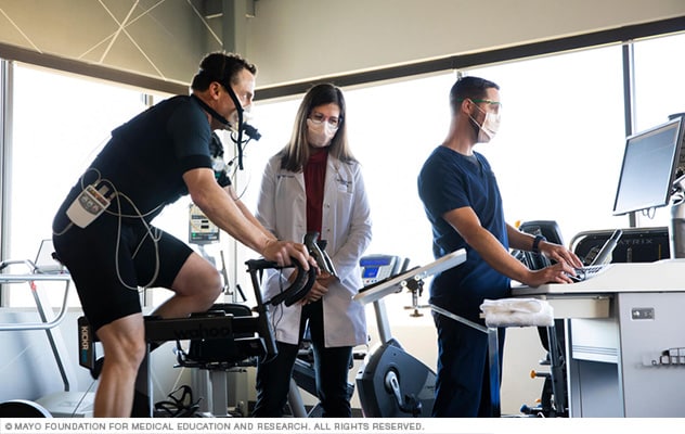 A man on a stationary cycle is monitored by medical staff.