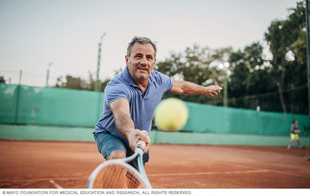 A tennis player stretches with racket in hand to return the ball.