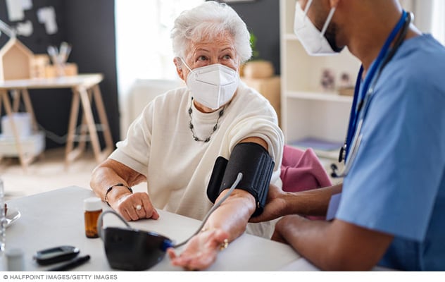 مريضة تنظر إلى ممرض رعاية منزلية أثناء قياس ضغط الدم.