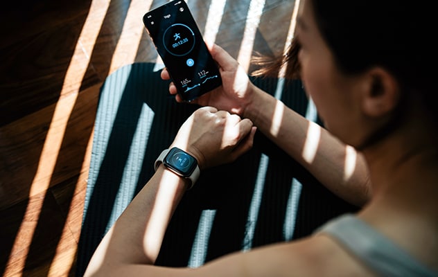 A person enrolled in concierge medicine optional services while sitting on a mat and checking their smartwatch and phone fitness data