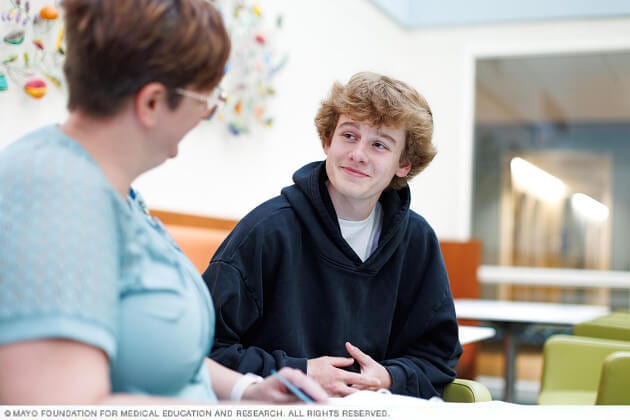 A young man and his therapist chat with one another at a table.