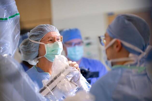 Two surgeons perform a procedure with controls visible.