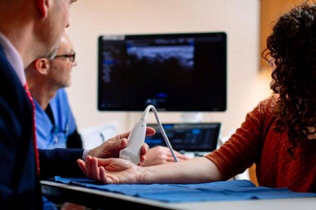 A doctor and a technician use ultrasound to examine a patient's wrist.