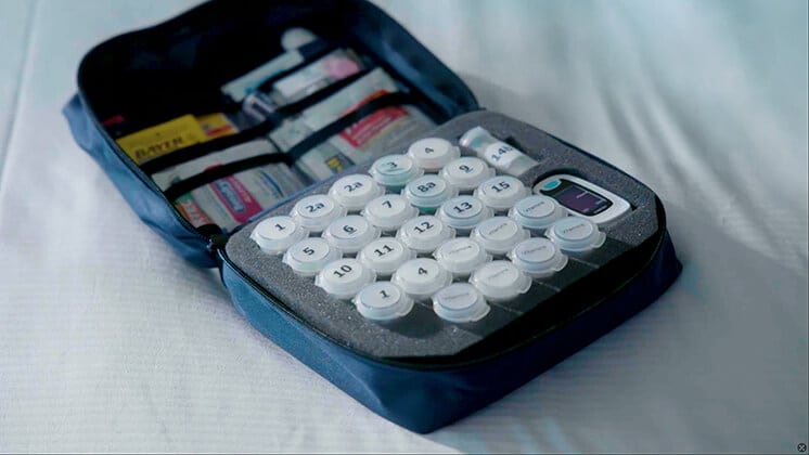 Personalized medical kit with numbered pill containers, a digital device, and medical supplies organized in a blue zippered case.