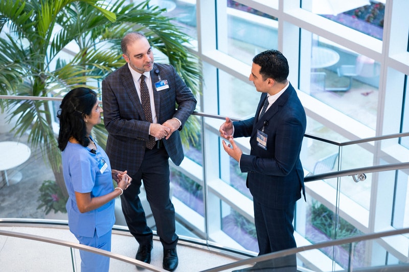 Two Mayo Clinic doctors and a nurse confer while standing on a staircase in a lobby area.