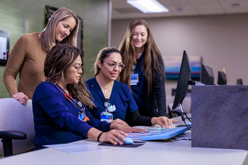 Four nurses working on an activity together at a nurse's station desk.