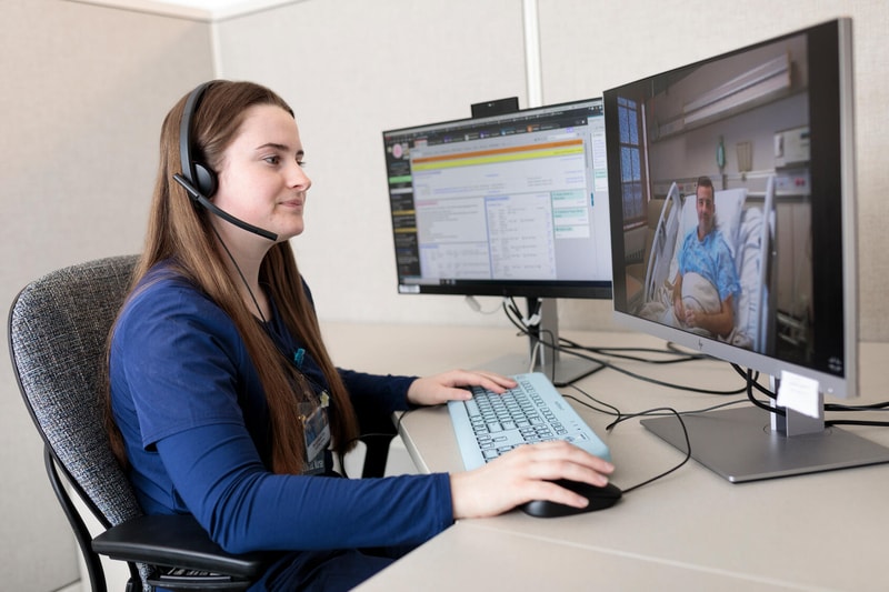A Mayo Clinic nurse does remote patient monitoring using two computer screens. One screen shows the patient and the other shows the patient's chart.