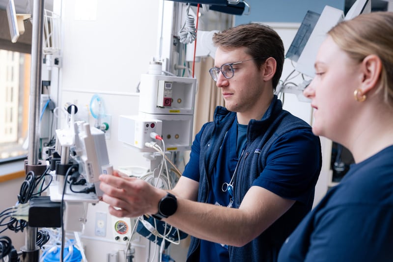Two Mayo Clinic nurses work together using medical equipment in a hospital room.