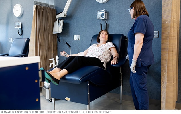 A person sits in a reclining chair with a needle inserted in the person's arm. The needle is attached to a thin, plastic tube and a blood bag.