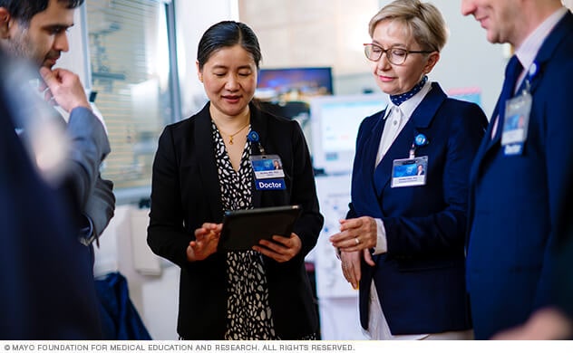 Mayo Clinic doctors talking with each other, while reviewing patient information on a tablet, in a clinical setting.
