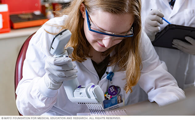Nephrology researcher in a lab uses pipette to test samples in a tray.