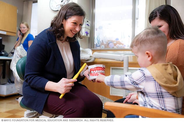 A pediatric dental specialist shows a child a model of teeth and a toothbrush during a visit.