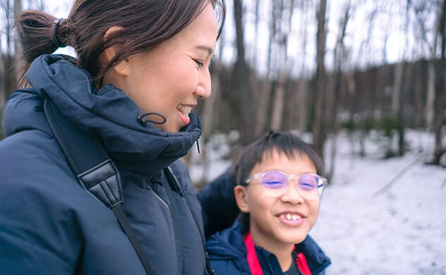 A mother and child walk through the woods in winter.