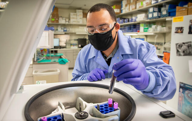 Photograph showing a masked technician in a lab handling test tubes