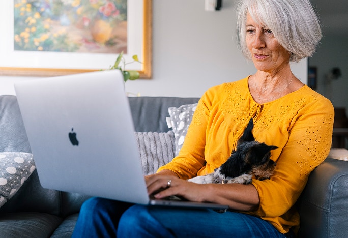 woman holding dog and using laptop on couch