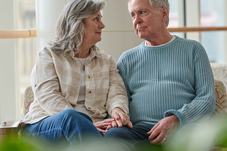 Older adult couple sat on a couch holding hands